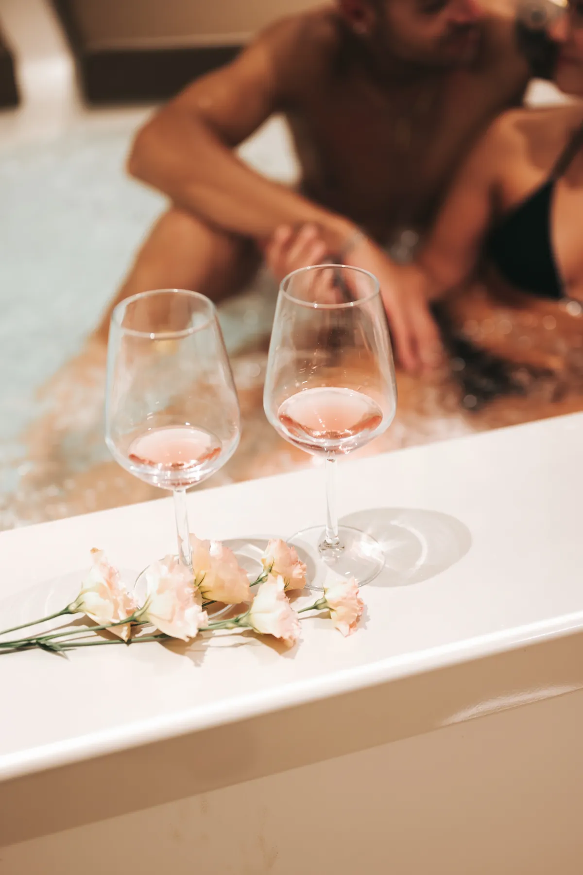 Calici di rosé e fiori sul bordo della vasca idromassaggio della Suite